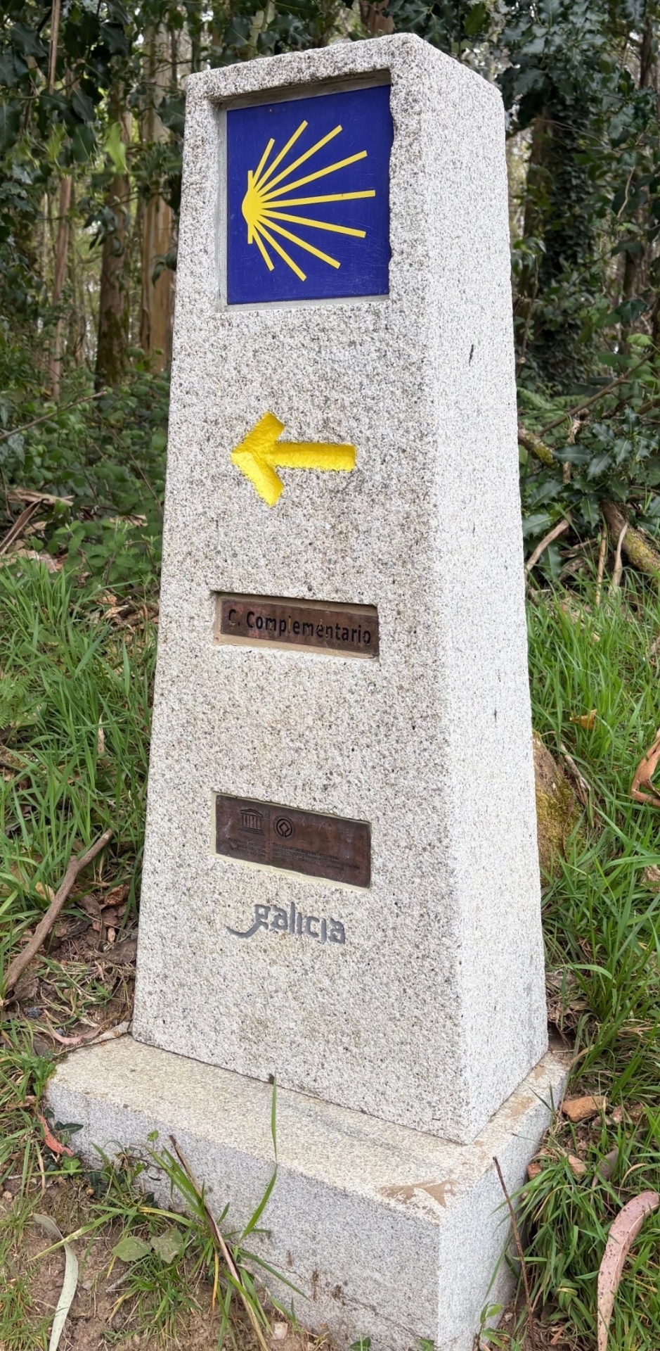 Stone Camino de Santiago waymarker with a yellow scallop shell and a yellow directional arrow